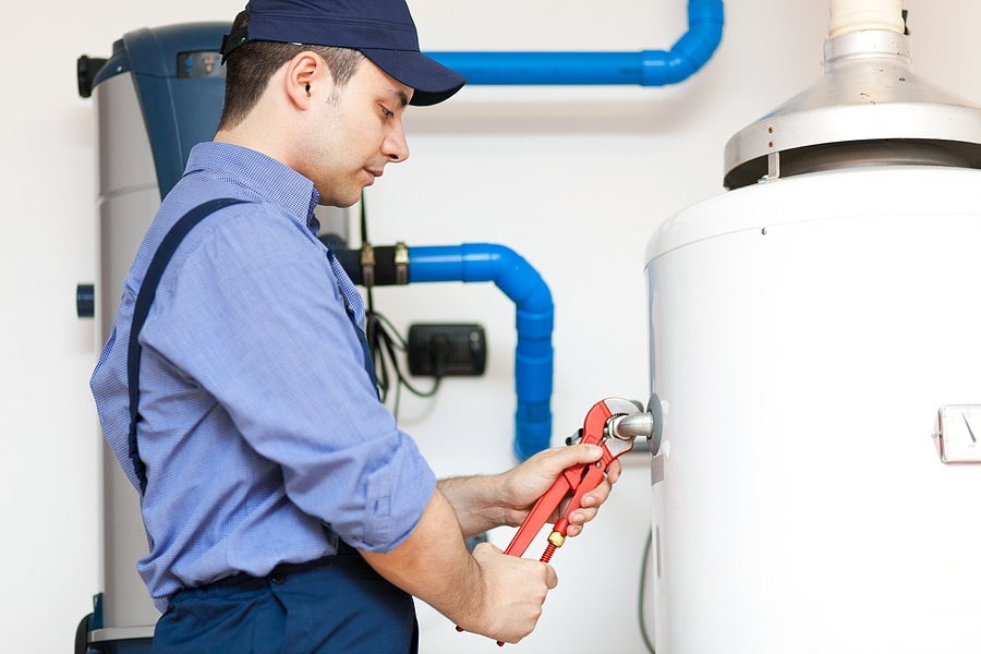 Technician in blue uniform servicing a hot-water heater for springtime maintenance.